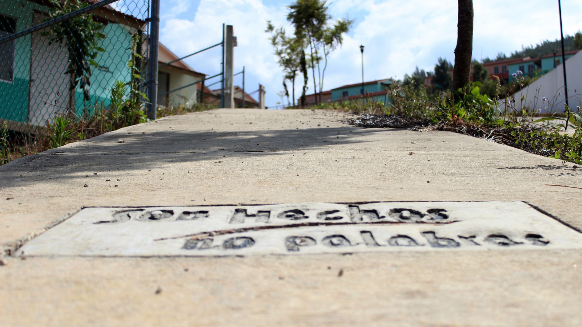 The imprint 'Deeds, not words' sits on the sidewalk in front of an abandonded house in the Sustainable Rural City of Santiago el Pinar. (Photo by Andrea Martinez.)