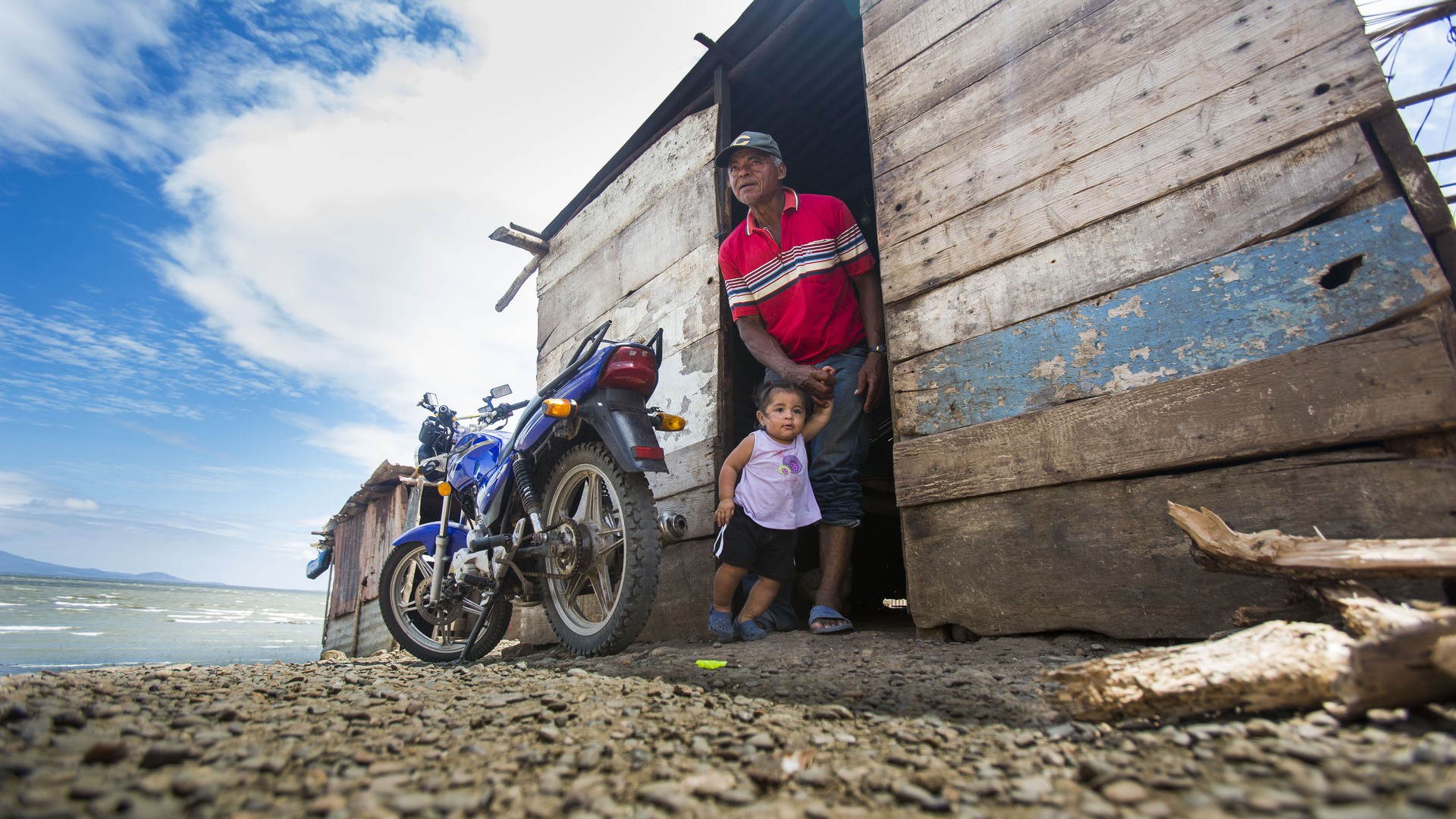 Gilberto Espinoza leads out his granddaughter, Cristhel, 2, out of the Espinozas' kitchen, which sits conveniently on the coast of Lake Nicaragua. According to Anatoña Duran, many of the residents do not have legal land rights to the homes that they live in. This will result in the displacement of the residents in Obrajuelo.  (Photo by Dominic Valente)