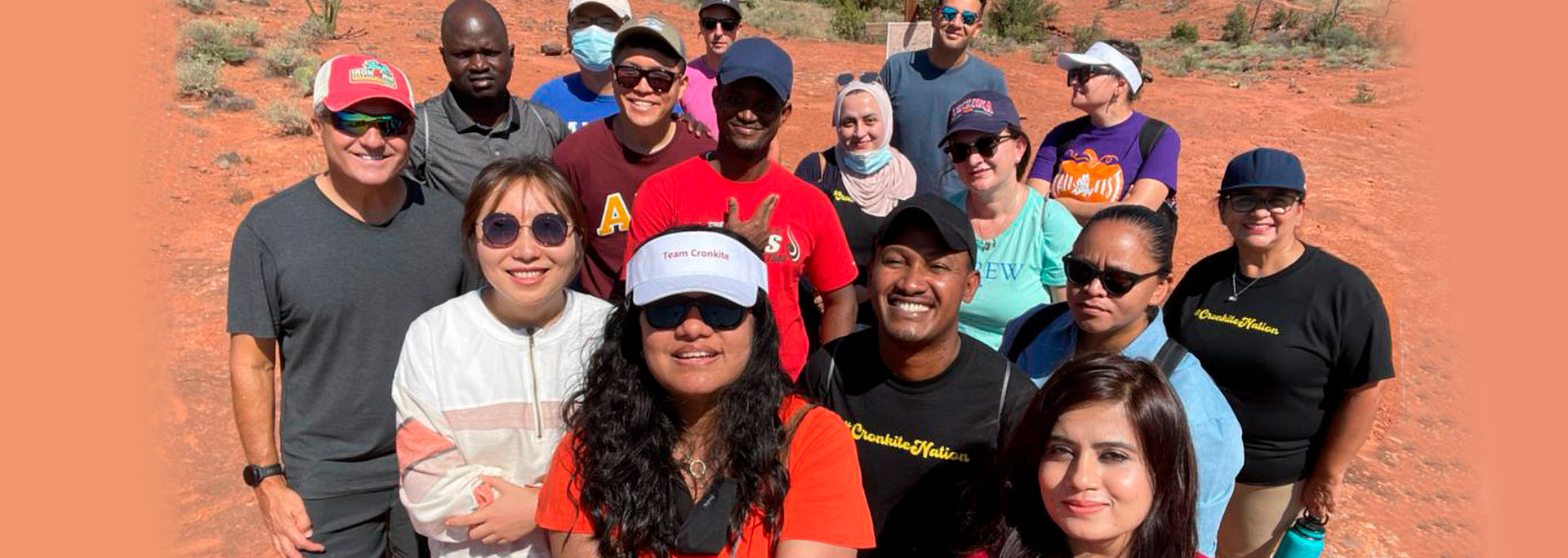 Group of people posing outdoors on a red dirt ground with clear skies in the background.