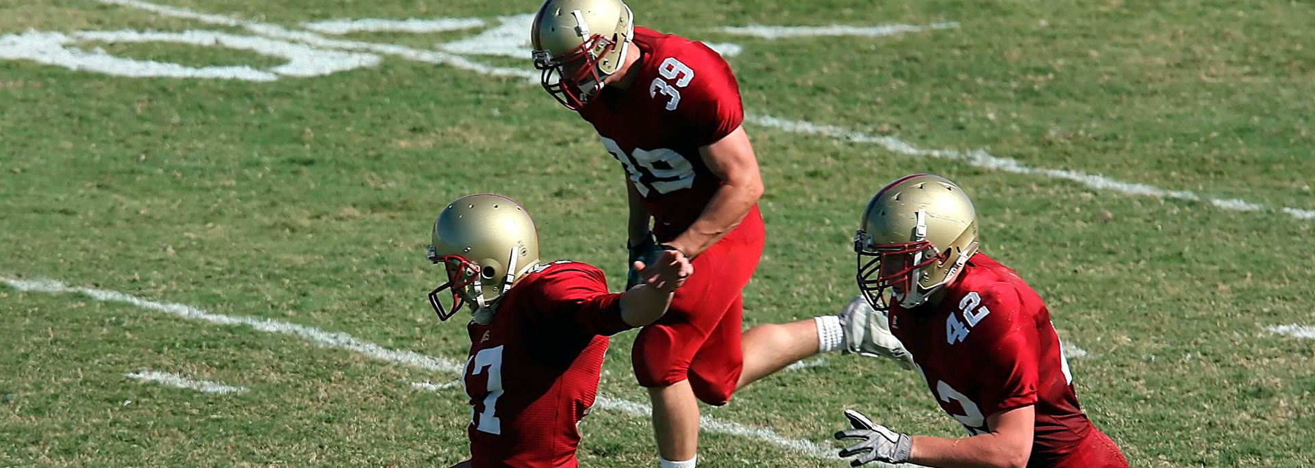 Football player in red uniform kicks the ball as another player runs next to him on a grassy field.