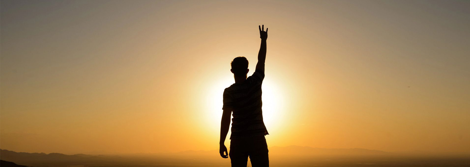 A student holds up the pitchfork hand symbol at sunset.