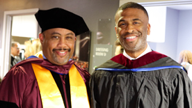 Two individuals in graduation regalia stand side by side.