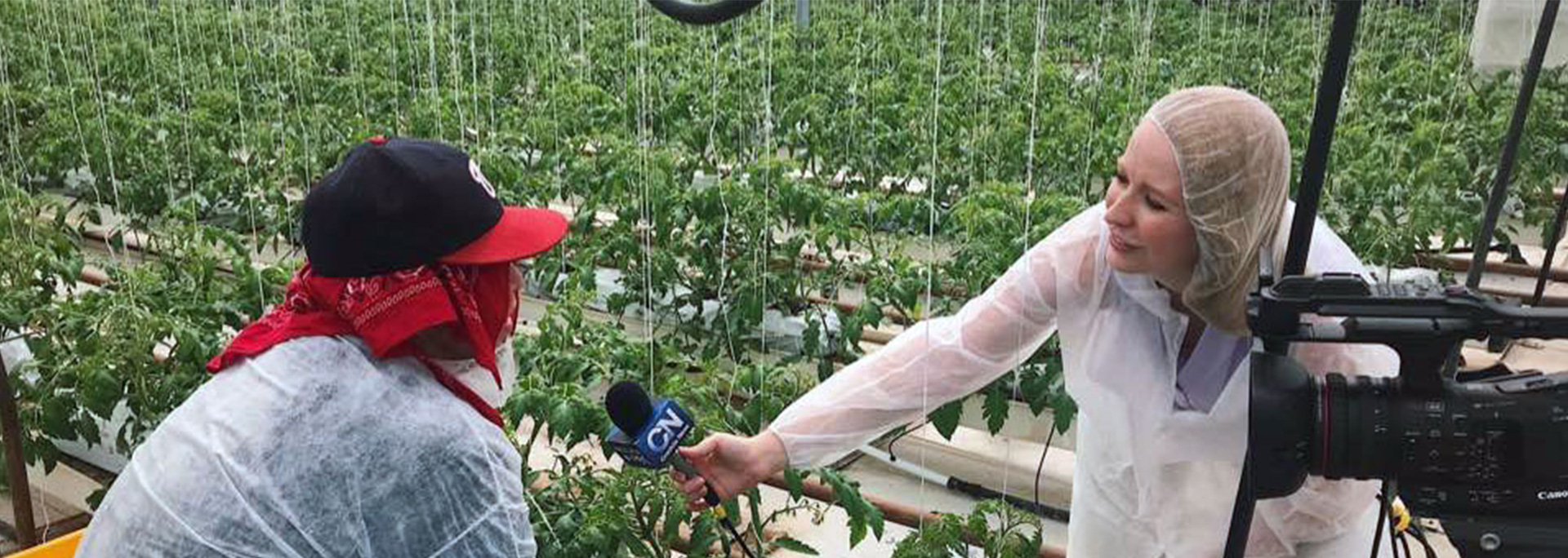 A student reporter interviews a worker outdoors in a field.