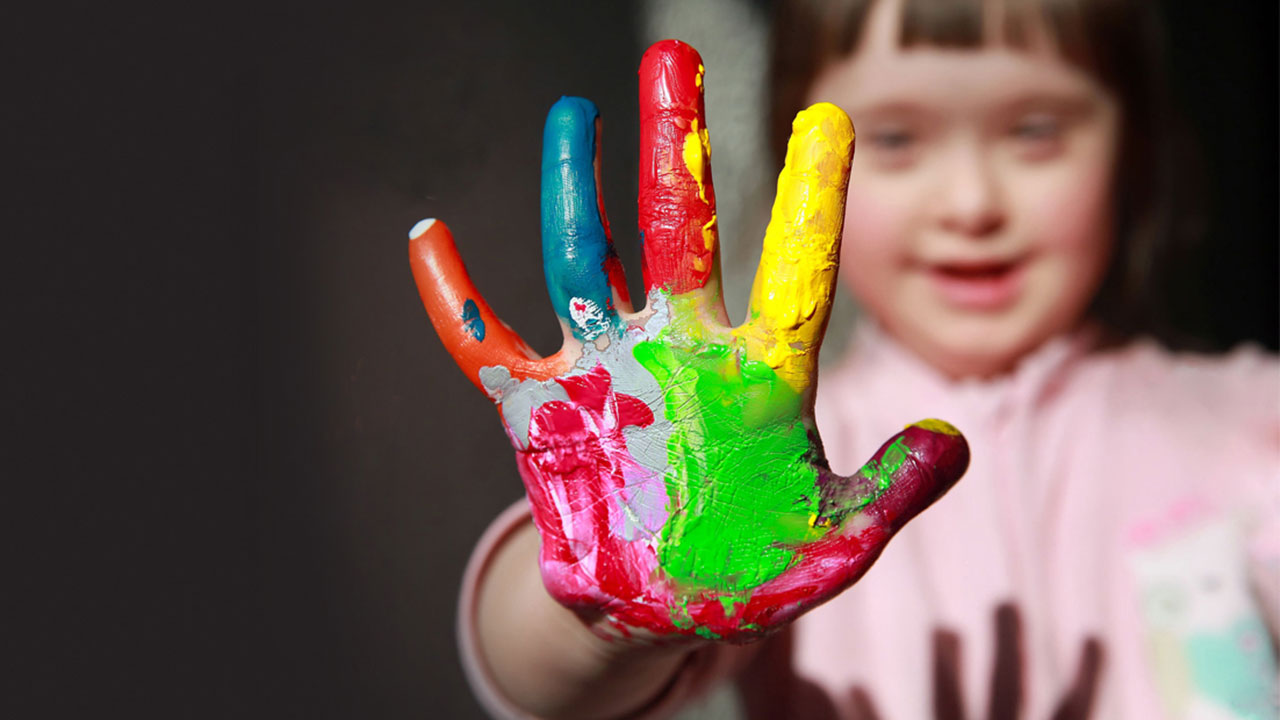 A girl a person who has Down syndrome with her hand out painted colorfully.