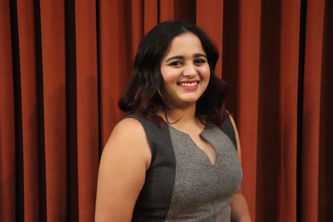 Nisha Sridharan stands in front of a maroon curtain